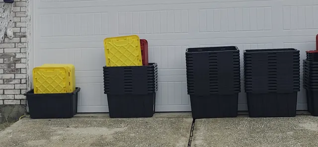 Stacks of Bin & Back rental moving boxes with yellow and red lids lined up in front of a Houston garage